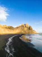 Northern scenery along ocean shore with massive Vestrahorn mountain peaks in Iceland. Famous Stokksnes seashore with icelandic black sand beach and nordic surroundings, natural skyline. photo