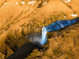 Aerial view of large waterfall in Iceland with stream pouring down from frozen terrain, wintry scenic route. Incredible icelandic landscape formed by majestic Skgafoss cascade in nordic region. photo