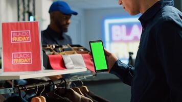 Adult with greenscreen on black friday event looking at clearance items, busy clothing store during seasonal sales. Man using isolated copyspace display in shopping center, bargain hunting. photo