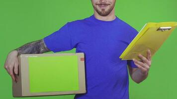 Cropped shot of a professional deliveryman smiling cheerfully delivering postal order holding cardboard box with copyspace and clipboard on green background profession employee post concept. video