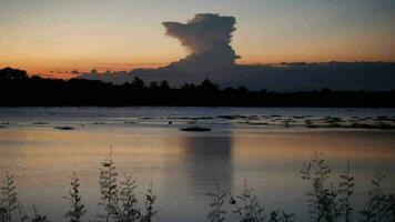 des nuages plus de lac, une vibrant le coucher du soleil plus de une serein lac, avec coloré reflets chatoyant sur le eau, Naturel paysage plus de une courant fonctionnement à rivière avec forêt et Montagne video