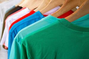 Fashion T-shirt on clothing rack - Closeup of bright colorful closet on wooden hangers in store closet. photo