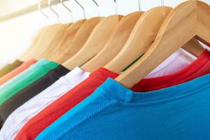 Moda camiseta en ropa estante - de cerca de brillante vistoso armario en de madera perchas en Tienda armario. foto