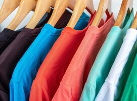 Fashion T-shirt on clothing rack - Closeup of bright colorful closet on wooden hangers in store closet. photo