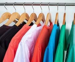 Fashion T-shirt on clothing rack - Closeup of bright colorful closet on wooden hangers in store closet. photo