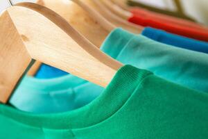 Fashion T-shirt on clothing rack - Closeup of bright colorful closet on wooden hangers in store closet. photo