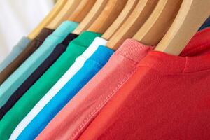 Moda camiseta en ropa estante - de cerca de brillante vistoso armario en de madera perchas en Tienda armario. foto