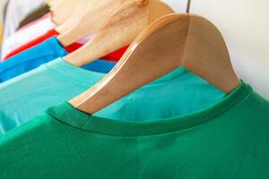 Fashion T-shirt on clothing rack - Closeup of bright colorful closet on wooden hangers in store closet. photo