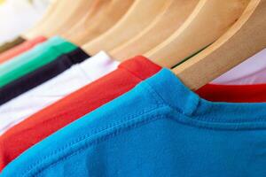 Fashion T-shirt on clothing rack - Closeup of bright colorful closet on wooden hangers in store closet. photo