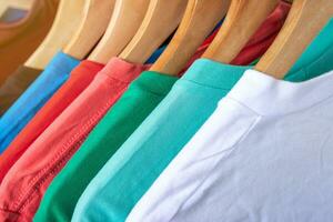 Fashion T-shirt on clothing rack - Closeup of bright colorful closet on wooden hangers in store closet. photo