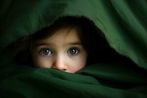 retrato de un linda pequeño niña ocultación debajo un verde frazada, linda pequeño bebé niña es ocultación debajo un verde cobija en cama, ai generado foto