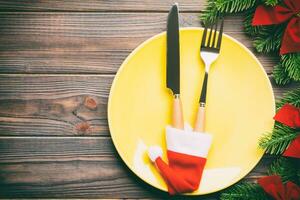 Holiday composition of plate and flatware decorated with Santa hat on wooden background. Top view of Christmas decorations with empty space for your design. Festive time concept photo