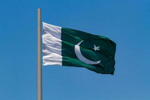 Flag of Pakistan waving in the wind on a pole against blue sky photo