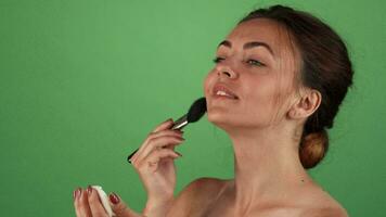 Gorgeous young woman applying makeup on green background video