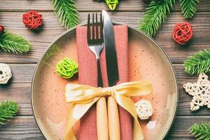 Holiday composition of plate and flatware decorated with Santa hat on wooden background. Top view of Christmas decorations. Festive time concept photo