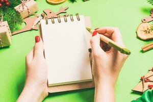 Top view of female hand making some notes in noteebok on green background. New Year decorations and toys. Christmas time concept photo