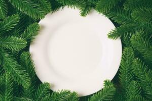 Top view of white plate surrounded with fir tree branches. Christmas dinner concept with copy space photo