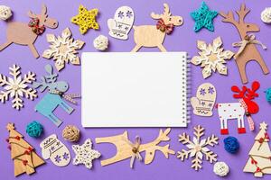 Festive decorations and toys on purple background. Top view of notebook. Merry Christmas concept photo