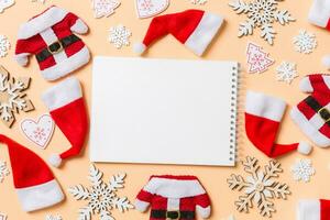 Top view of notebook with Christmas decorations and Santa hats on orange background. Happy holiday concept photo