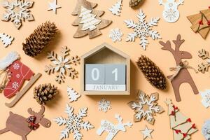 Top view of wooden calendar surrounded with New Year toys and decorations on orange background. The first of January. Christmas time concept photo