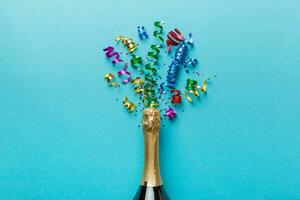 Creative flat lay composition with bottle of champagne and space for text on color background. Champagne bottle with colorful party streamers. holiday or christmas concept photo