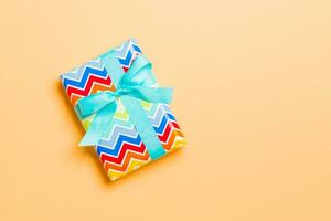 wrapped Christmas or other holiday handmade present in paper with blue ribbon on orange background. Present box, decoration of gift on colored table, top view with copy space photo