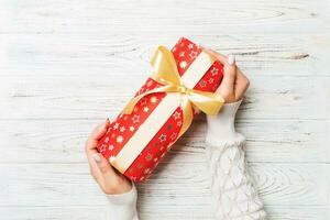 Woman hands give wrapped christmas or other holiday handmade present in colored paper . Present box, decoration of gift on white rustic wooden table, top view with copy space photo