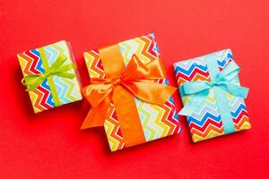 wrapped Christmas or other holiday handmade present in paper with blue, green and orange ribbon on red background. Present box, decoration of gift on colored table, top view photo