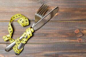Diet and healthy eating concept with crossed fork and knife and measuring tape on wooden background. Top view of weightloss photo