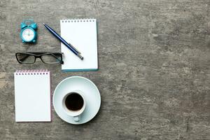 moderno oficina escritorio mesa con cuaderno y otro suministros con taza de café. blanco cuaderno página para usted diseño. parte superior vista, plano laico foto