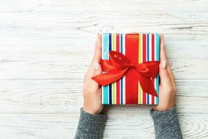 Woman arms holding gift box with colored ribbon on white rustic wooden table background, top view and copy space for you design photo