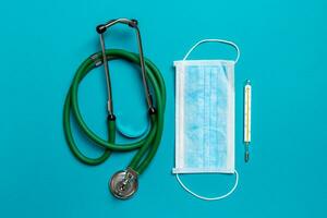 Top view of stethoscope, mercury thermometer and a protective face mask on colorful background. Medical equipment and health care concept photo