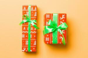 wrapped Christmas or other holiday handmade present in paper with green ribbon on orange background. Present box, decoration of gift on colored table, top view photo