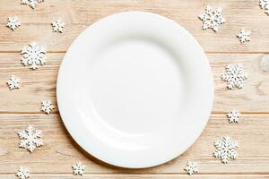 Top view of empty plate surrounded with snowflakes on wooden background. New Year dinner concept photo