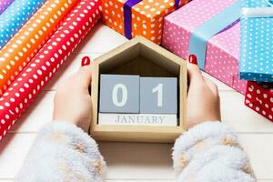 Top view of female hands holding a calendar on wooden background. The first of January. Holiday decorations. New Year concept photo