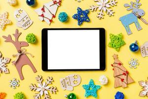 Top view of digital tablet on yellow background with New Year toys and decorations. Christmas time concept photo