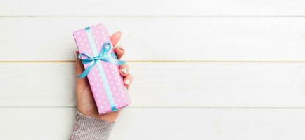 Female's hands holding striped gift box with colored ribbon on white rustic wooden background. Christmas concept or other holiday handmade present box, concept top view with copy space photo