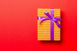 envuelto Navidad o otro fiesta hecho a mano presente en papel con púrpura cinta en rojo antecedentes. presente caja, decoración de regalo en de colores mesa, parte superior ver con Copiar espacio foto