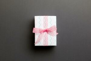 wrapped Christmas or other holiday handmade present in paper with pink ribbon on black background. Present box, decoration of gift on colored table, top view with copy space photo