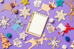 Festive decorations and toys on purple background. Top view of notebook. Merry Christmas concept photo