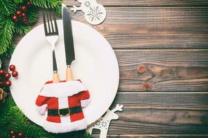 Top view of Christmas dinner on wooden background. Plate, utensil, fir tree and holiday decorations with copy space. New Year time concept photo