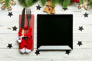 Top view of fork, knife and plate surrounded with fir tree and Christmas decoratoins on wooden background. New Year Eve and holiday dinner concept photo