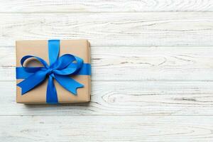 Holiday gift box wrapped in craft paper with colored bow on table background. Top view, flat lay, copy space photo