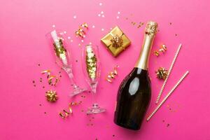 Bottle of champagne with colored glitter, confetti and gift box space for text on colorfull background, top view. Hilarious, christmas and birthday celebration photo