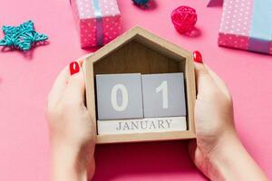 vista superior de las manos femeninas sosteniendo el calendario sobre fondo rosa. el primero de enero. decoraciones navideñas. concepto de año nuevo foto