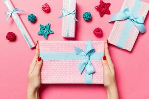 Top view of female hands holding a Christmas present on festive pink background. Holiday decorations, toys and balls. New Year holiday concept photo