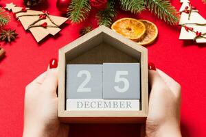 Top view of female hands holding calendar on red background. The twenty fifth of December. Holiday decorations. Christmas time concept photo