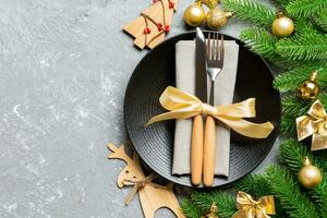 Top view of New Year dinner on festive cement background. Composition of plate, fork, knife, fir tree and decorations. Merry Christmas concept photo