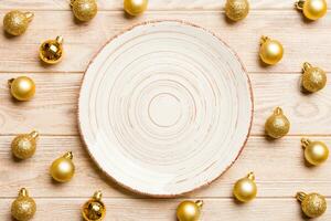 Top view of festive plate with golden baubles on wooden background. Christmas decorations and toys. New Year advent concept photo