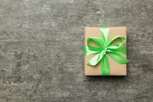 Holiday gift box wrapped in craft paper with colored bow on table background. Top view, flat lay, copy space photo